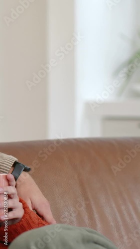 Vertical video: She in orange knit holding mug at home mate placing arm to support, band