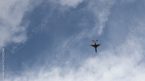 Obraz na plátně Single jet flying overhead through blue sky and wispy clouds