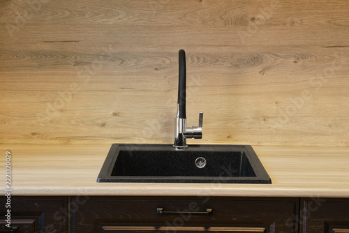Sink is placed in kitchen on wooden countertop. Faucet is shiny and modern. Background has smooth wooden texture.