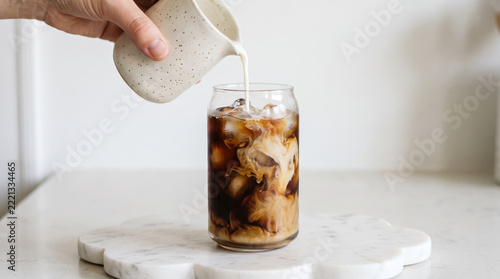 Pouring milk into a glass of iced coffee on a marble surface