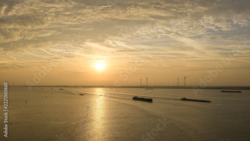 Boats navigating Ooltgensplaat river with wind turbines at sunrise