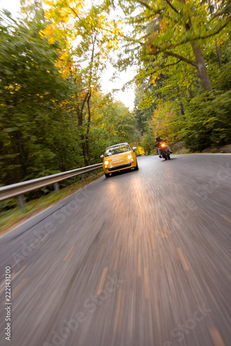 Motorcyclist Overtaking a Small Yellow Car on a Forest Road