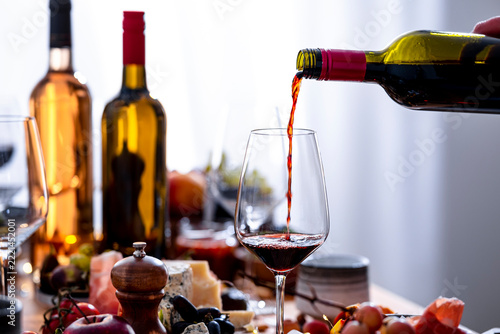 Red wine Rioja pouring into tall glass during autumn lunch. Gourmet food pairing concept with cheese platter. Elegant festive celebration event with crystal glassware and fresh grapes.
