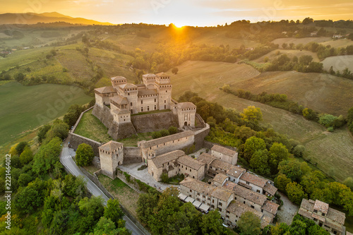 Aerial view of Torrechiara Castle and village on a hilltop at golden hour with sun flare over the Parma countryside