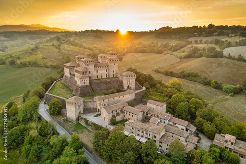 Aerial view of Torrechiara Castle and village on a hilltop at golden hour with sun flare over the Parma countryside