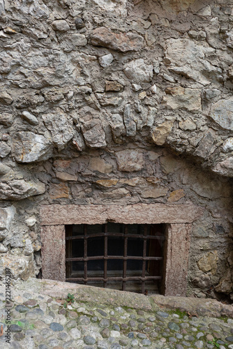 Small barred cellar window with rustic stone arch and masonry wall in the medieval village of Canale di Tenno, Italy.
