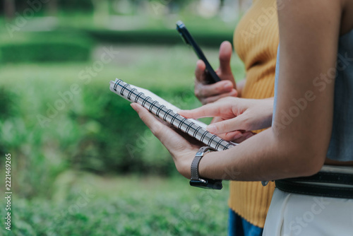 Young Asian Woman and Mature Woman Sharing Knowledge While Reading a Notebook Outdoors in a Park