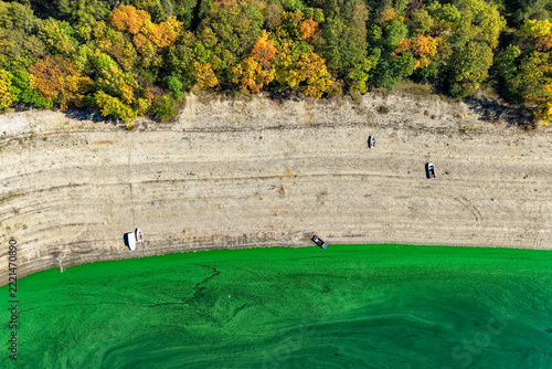 Exposed rocky shoreline with small boats, colorful autumn forest and unusual green reservoir water
