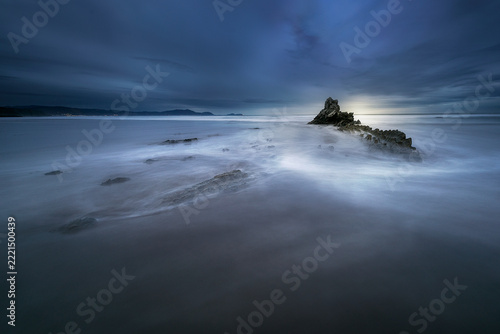 Rocky flysch formation on beach shore during blue hour with silky long exposure sea water, Sopelana beach in Bizkaia, Cantabrian sea, Spain
