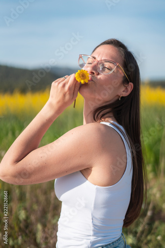 Young woman smelling a yellow flower in a sunny meadow during spring