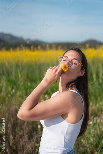 Young woman smelling a yellow flower in a sunny meadow during a