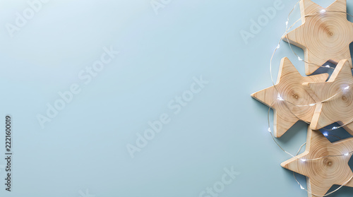 Wooden star ornaments with fairy lights on light blue background, festive Christmas star decorations with copy space, rustic wooden stars festive flat lay