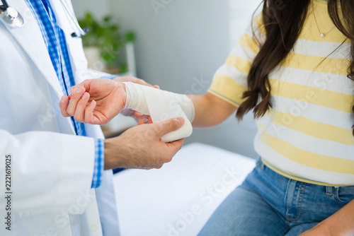 Closeup of a doctor carefully applying a white elastic bandage to a patient's injured wrist for first aid and recovery in a medical office