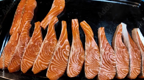 Close up shot of fresh raw salmon fish steaks arranged in a row on a black display surface at a street food market stall in Thailand.
