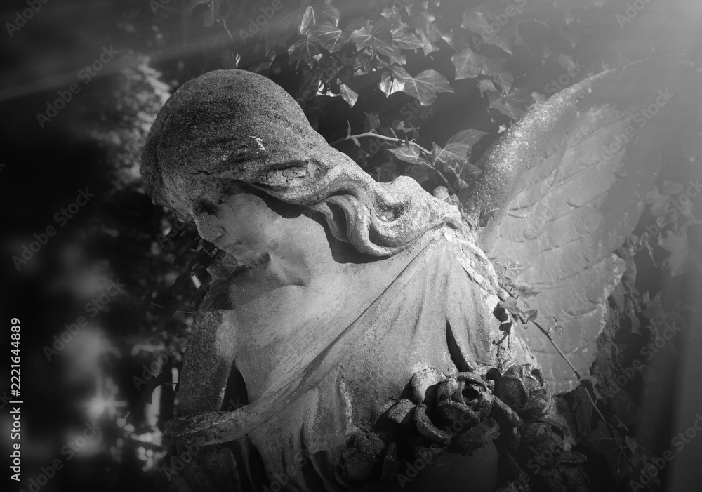 Fototapeta premium Stone angel holding roses illuminated by heavenly light, symbolizing hope, remembrance, eternal peace and the journey of the soul to heaven.