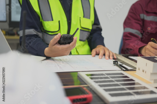 Worker, radio, vest, blueprint, model, desk during indoor construction planning with reflective safety clothing