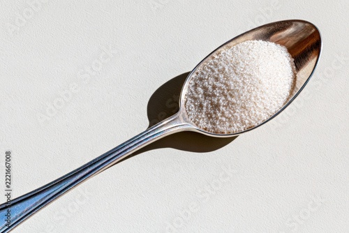 Close-up of teaspoon filled with granulated sugar casting a warning shadow about health risks of sugar consumption