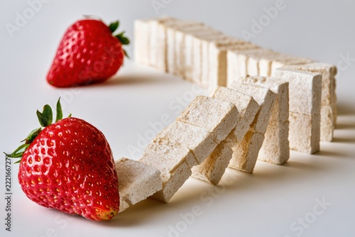 Long row of sugar cubes falling like dominoes with a strawberry in a studio setting