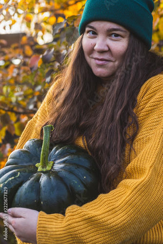 A woman in an orange sweater holds a green pumpkin in her hands