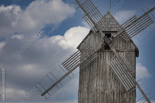 Rustic wooden windmill standing against a dramatic blue sky with fluffy white summer clouds