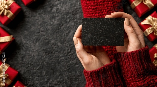 Female hands holding a blank black card surrounded by red gift boxes with gold ribbons