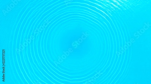 Concentric ripples emanate outward from a central point across a vibrant azure liquid surface, creating hypnotic circular wave patterns that suggest motion and a serene natural phenomenon