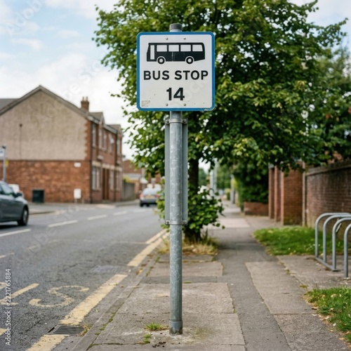 Urban bus stop sign with route number 14 on a sidewalk next to a street with trees and houses