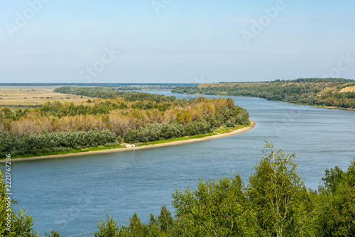 Green, forest-clad banks frame the wide river, which winds calmly in an intricate pattern;