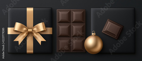 A luxurious dark chocolate bar and a beautifully wrapped gift box with a golden ribbon sit elegantly on a dark surface, accompanied by a festive golden bauble.