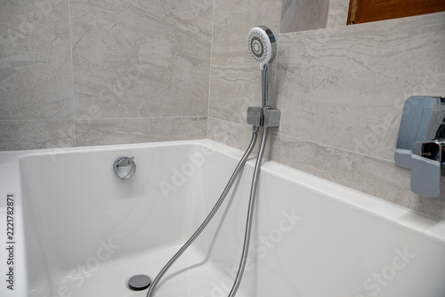 Modern white bathtub with handheld showerhead in elegant marble bathroom