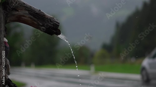 Fresh water flowing from wooden pipe with blurred car driving on road
