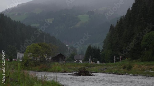 Wide shot of a mountain river flowing past dense pine forests and a highway with a passing truck in an alpine valley. Perfect for environmental, travel, nature, and logistics video projects