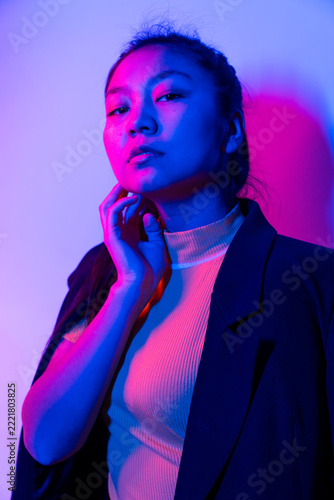 Studio portrait of a young Asian woman under blue and magenta neon lights.
