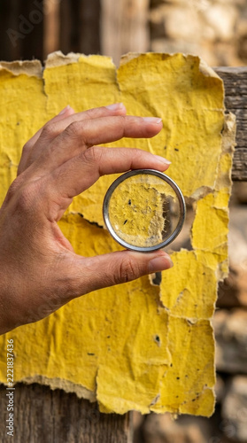 Hand holding magnifying glass examining rough textured yellow paper with torn edges close up
