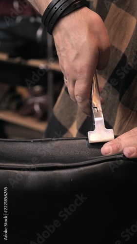 Close up of a leather artisan hands using leather pliers tool to shape black leather bag in workshop. Handcrafted leather goods, artisan craftsmanship, shoemaking and small business concept