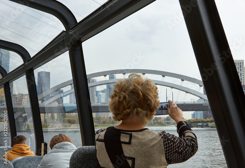 Wall Mural Woman photographing city skyline from river tram through windows with arched bri