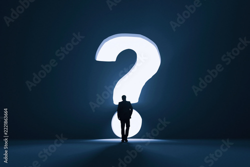 Fotografie Silhouette of a businessman standing in front of a massive glowing question mark portal in a dark room, facing uncertainty, searching for business solutions, answers, choices, and future direction