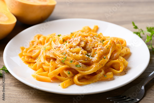Butternut squash pasta topped with grated parmesan cheese and fresh herbs on white plate, Autumn seasonal food