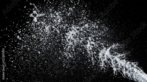 A stream of clear water splashing and spraying across a dark black background with powerful jet water sprays outward transparent
