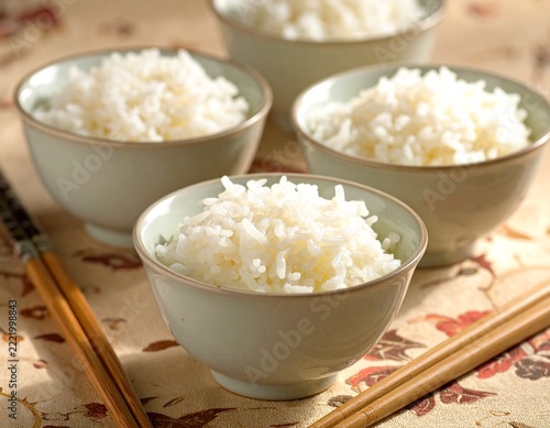 Small ceramic bowls holding freshly cooked white rice with chopsticks on a decorative