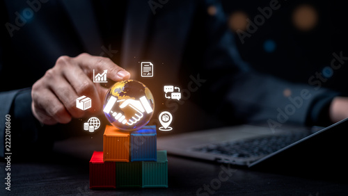 Global business partnership and logistics trade concept. Businessman touching virtual globe with handshake, graph, document and shipping icons above colorful toy cargo containers.
