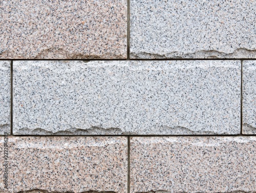 Close-up of a textured stone wall showing rectangular blocks with a speckled surface and slight chipping along the edges.