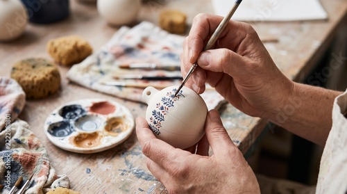 Artisan painting botanical details on a ceramic vase by hand.
