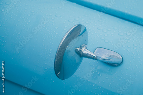 Close up of vintage blue car fender mirror covered in fresh raindrops.
A high-quality close-up photograph capturing the classic chrome round fender mirror of a vintage retro automobile. The glossy
