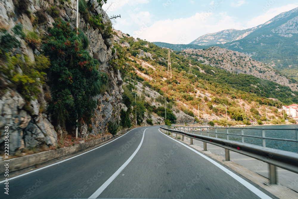 Fototapeta premium Curved road along rocky mountainside near water in daylight