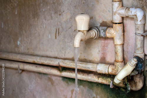 Old rusty water faucet and pipes with water flowing against a weathered wall