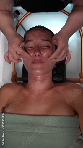 Professional cosmetologist massaging woman's cheeks at spa