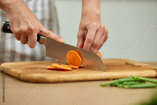 Person slicing carrots on wooden chopping board preparing food