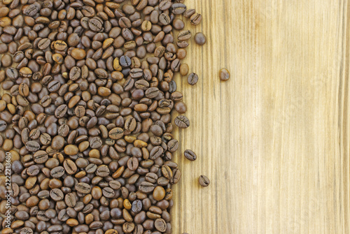 Top view of roasted coffee beans arranged along the left side of a light wooden background, creating a warm food and beverage texture with open space on the right