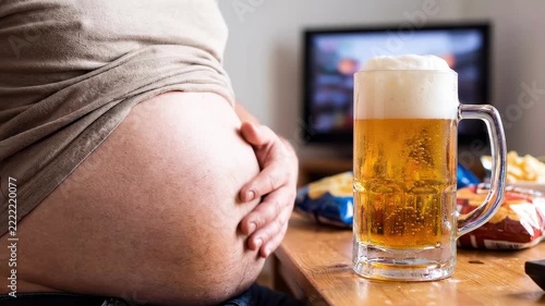 Overweight person with beer and snacks watching television at home.